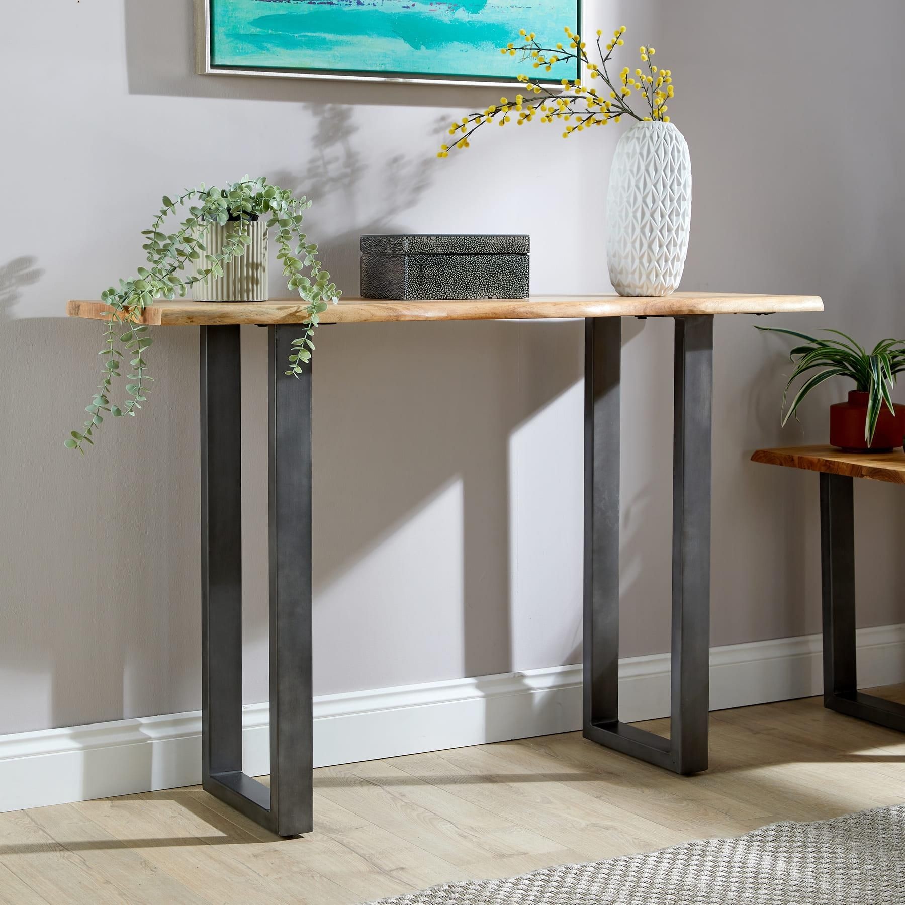 Live edge console table featuring a solid 26mm acacia wood top with natural grain, supported by sleek black metal legs, styled with decorative plants and a textured vase.