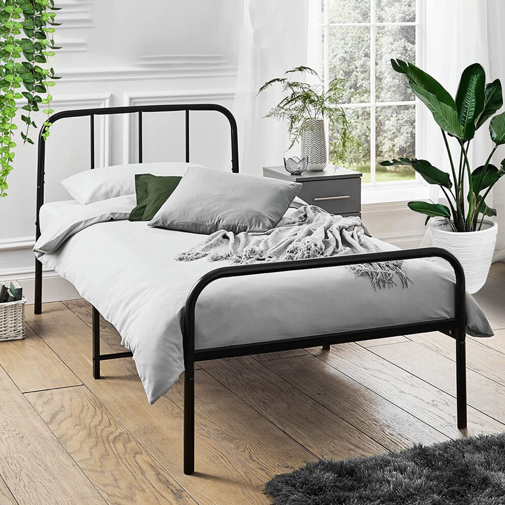Extra strong black metal bed frame featuring rounded head and footboards, complemented by light bedding and a cozy throw, set in a bright, plant-filled room.