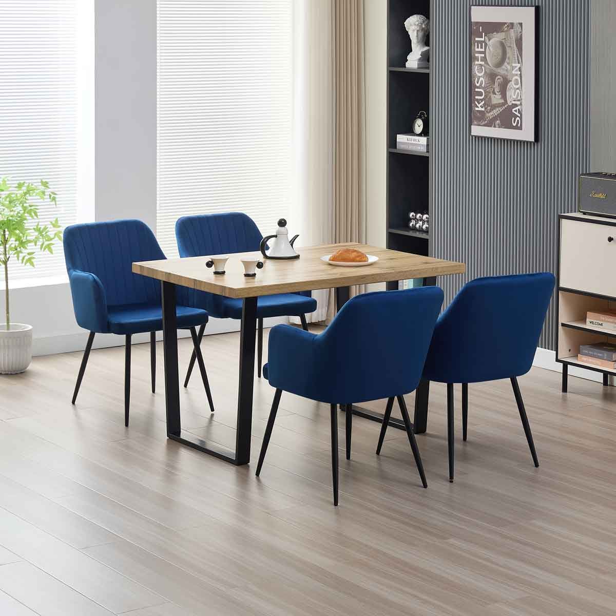 Colorado dining table with a light wood top and black metal legs, accompanied by four blue velvet Charlotte chairs with ribbed detailing.