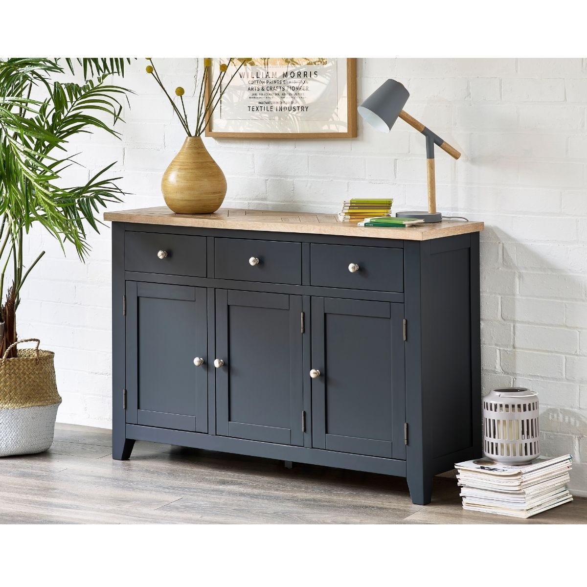 Dark grey wooden sideboard with a natural wood top, featuring three drawers and two cabinet doors, complemented by silver knobs and a stylish lamp on the surface.