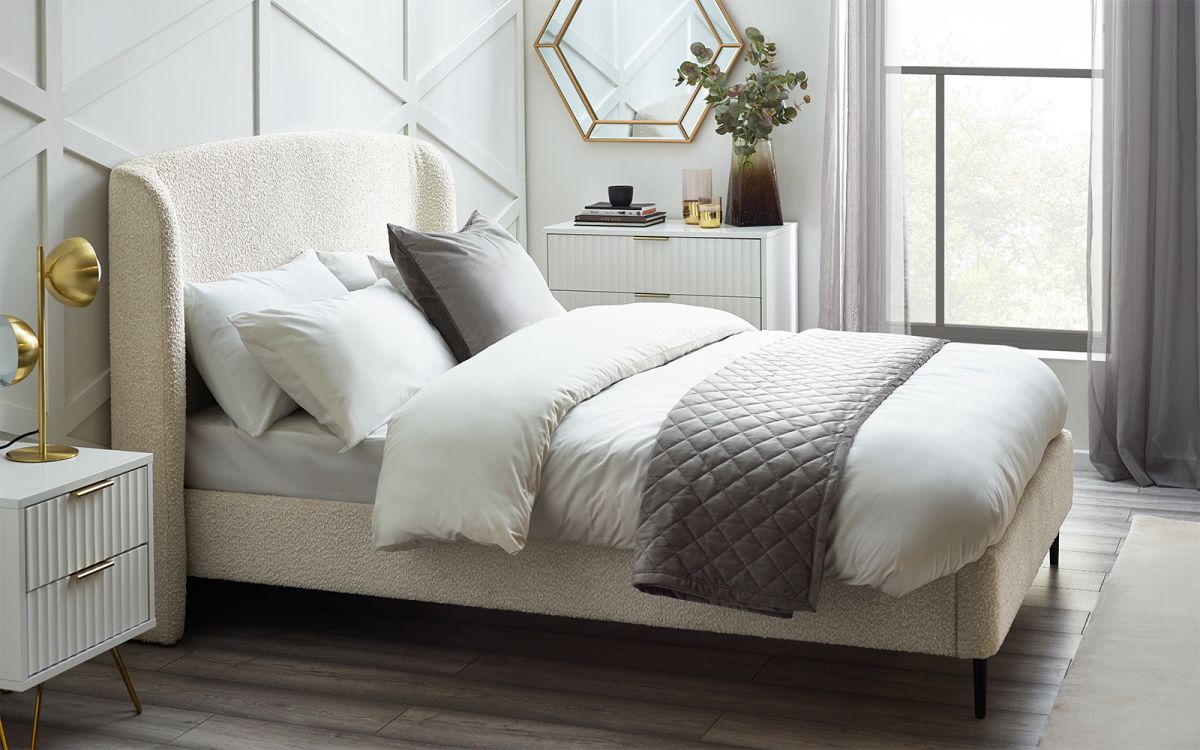 Cream boucle double bed frame with a curved headboard, complemented by plush white and gray bedding, set against a stylish, modern bedroom backdrop.