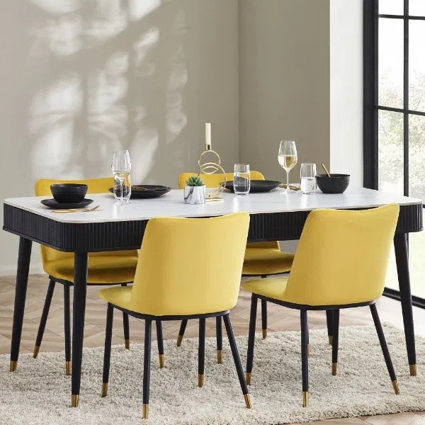 Black and white dining table with a fluted stone top, featuring two drawers, surrounded by four yellow upholstered chairs with black legs and gold accents.