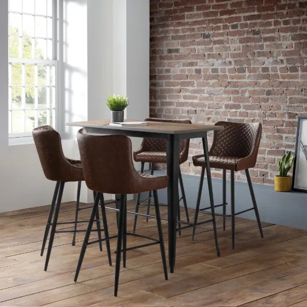 Brown faux leather barstool with a quilted backrest and black metal legs, set around a wooden table in a bright, modern room with exposed brick walls.