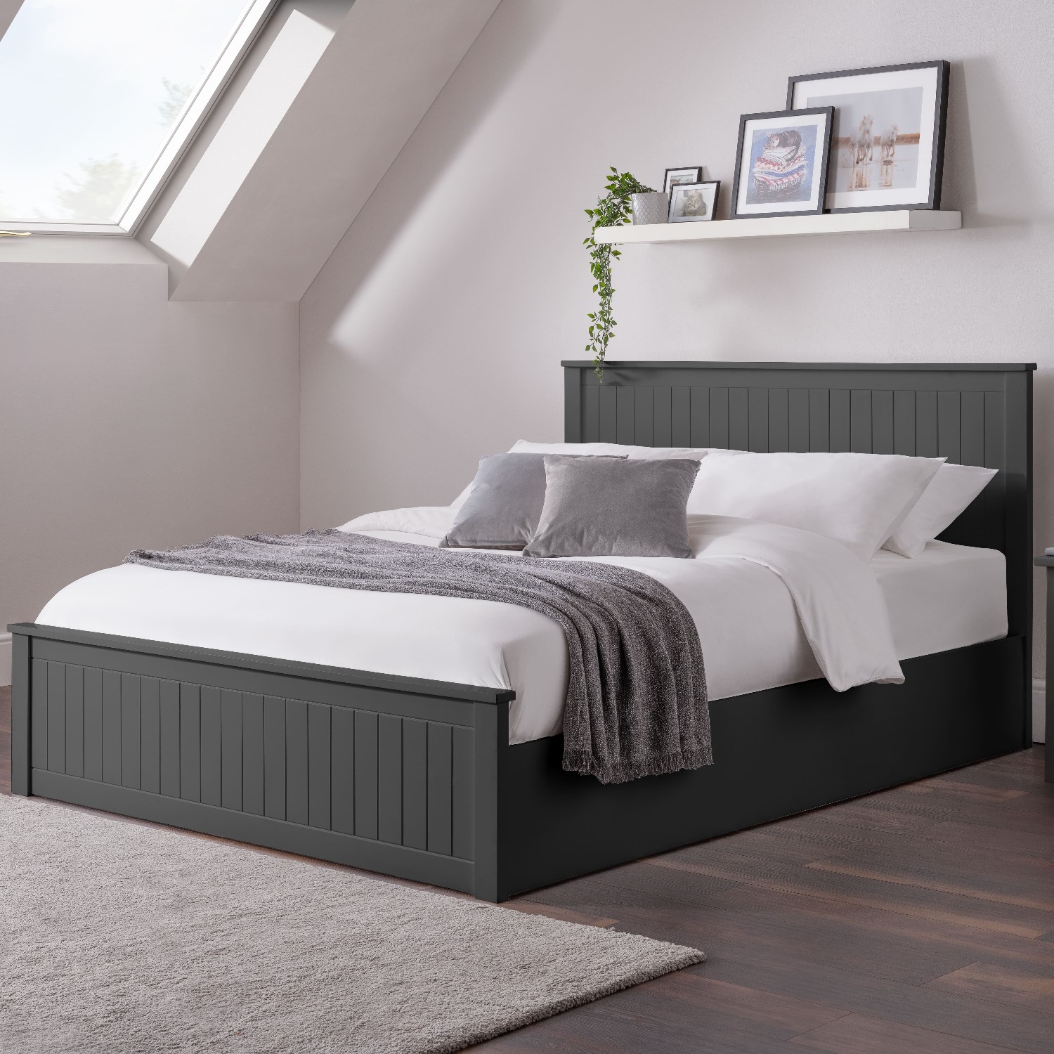 Anthracite-colored Julian Bowen Maine Ottoman bed with a slatted headboard, plush white bedding, and decorative pillows, set in a modern room with angled ceiling and natural light.