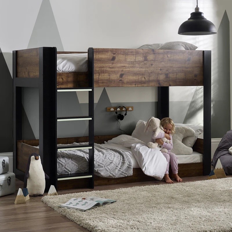 Rustic and black Julian Bowen Solomon bunk bed featuring a sturdy wooden frame, a ladder, and cozy bedding, with a child sitting on the lower bunk in a softly lit room.