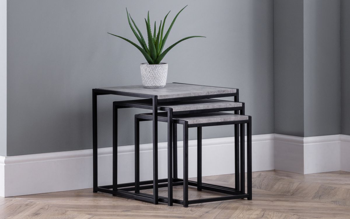 Nest of three tables featuring a concrete top and black metal frame, with a small potted plant on the largest table, set against a gray wall and wooden floor.