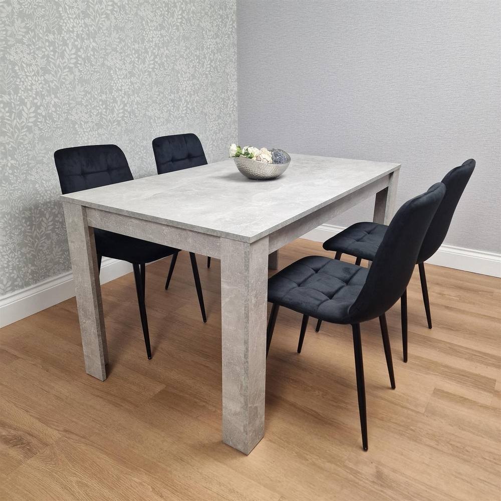 Modern grey dining table with a textured finish paired with four black velvet chairs featuring tufted backs and sleek black legs, set against a patterned wall.