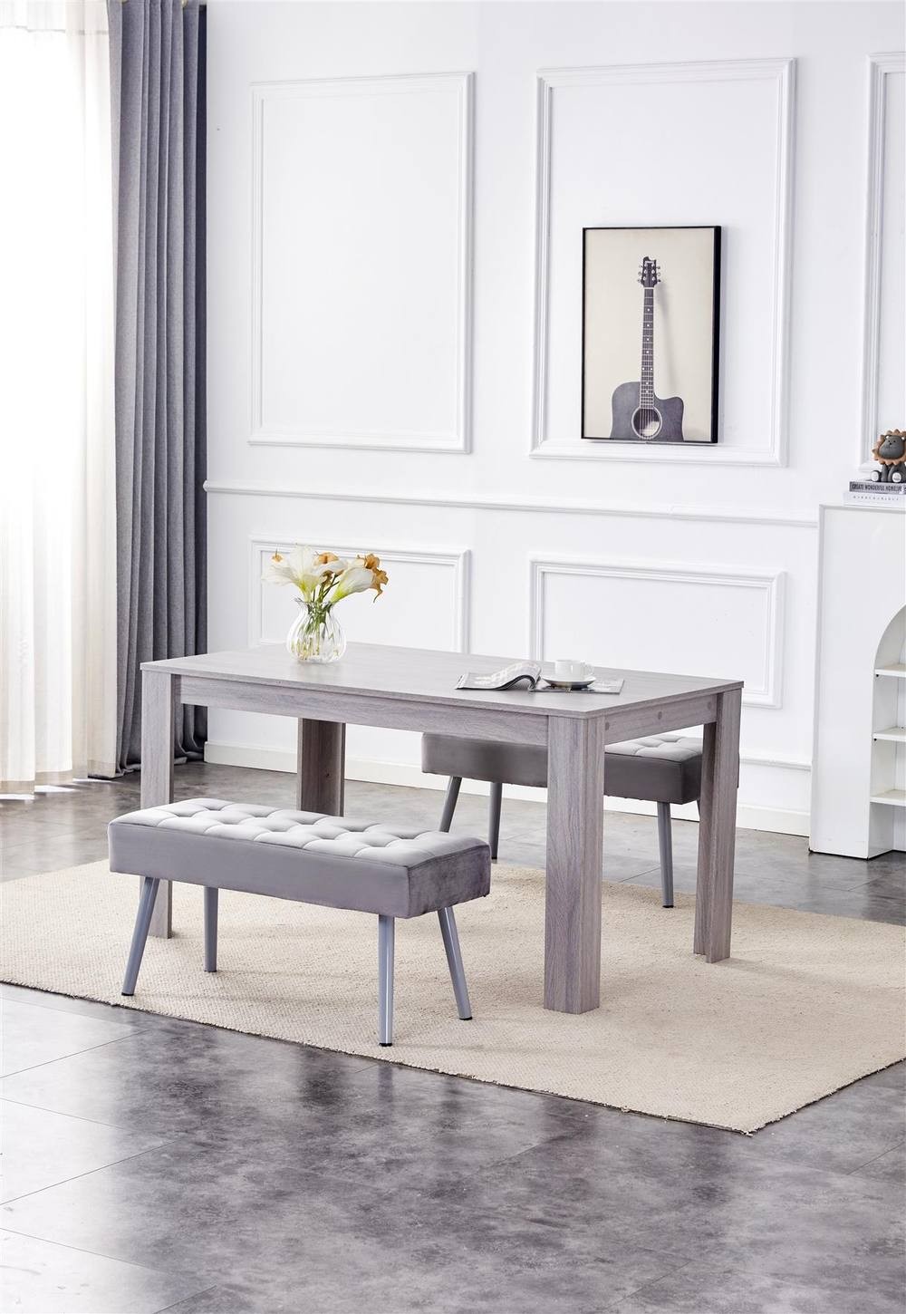 Grey velvet benches with tufted seats accompany a light wood dining table, set on a neutral rug in a bright, modern room with decorative wall art.