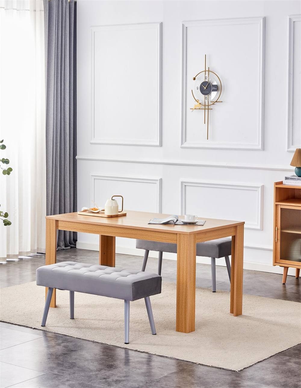 Oak effect wood dining table with two grey velvet benches, set in a stylish room with a light rug, curtains, and modern wall decor.