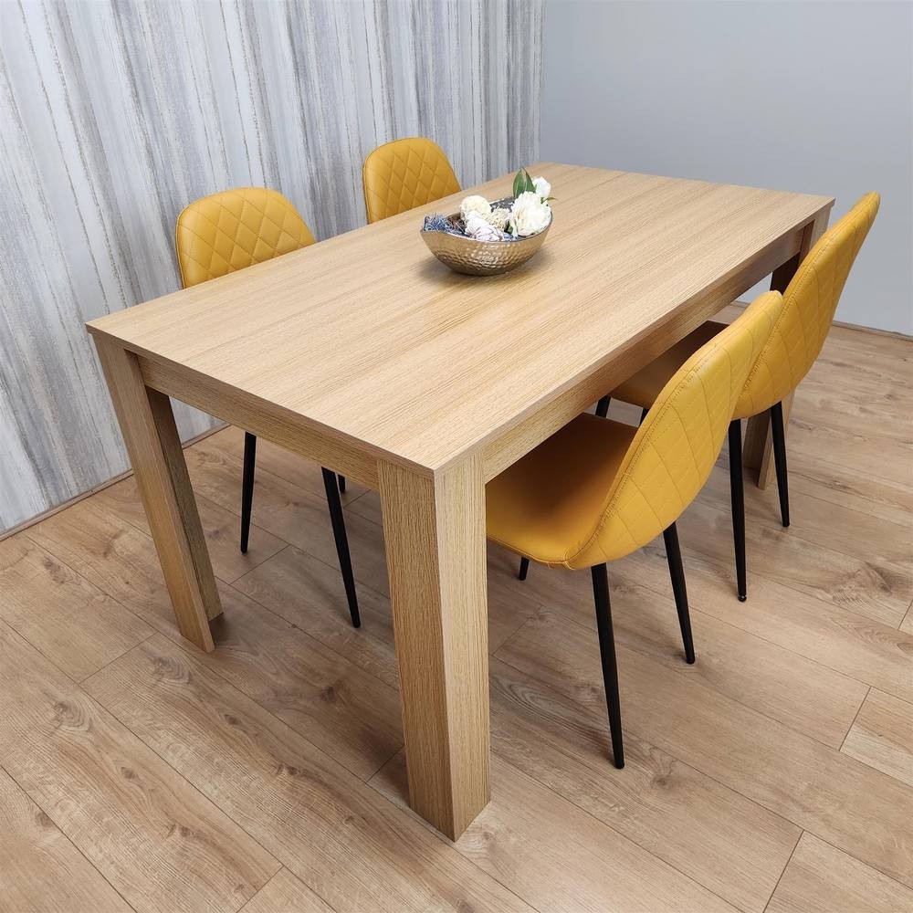 Oak effect dining table with four mustard gem patterned chairs in beige, featuring a sleek design and a rectangular shape, set against a light wooden floor and textured wall.