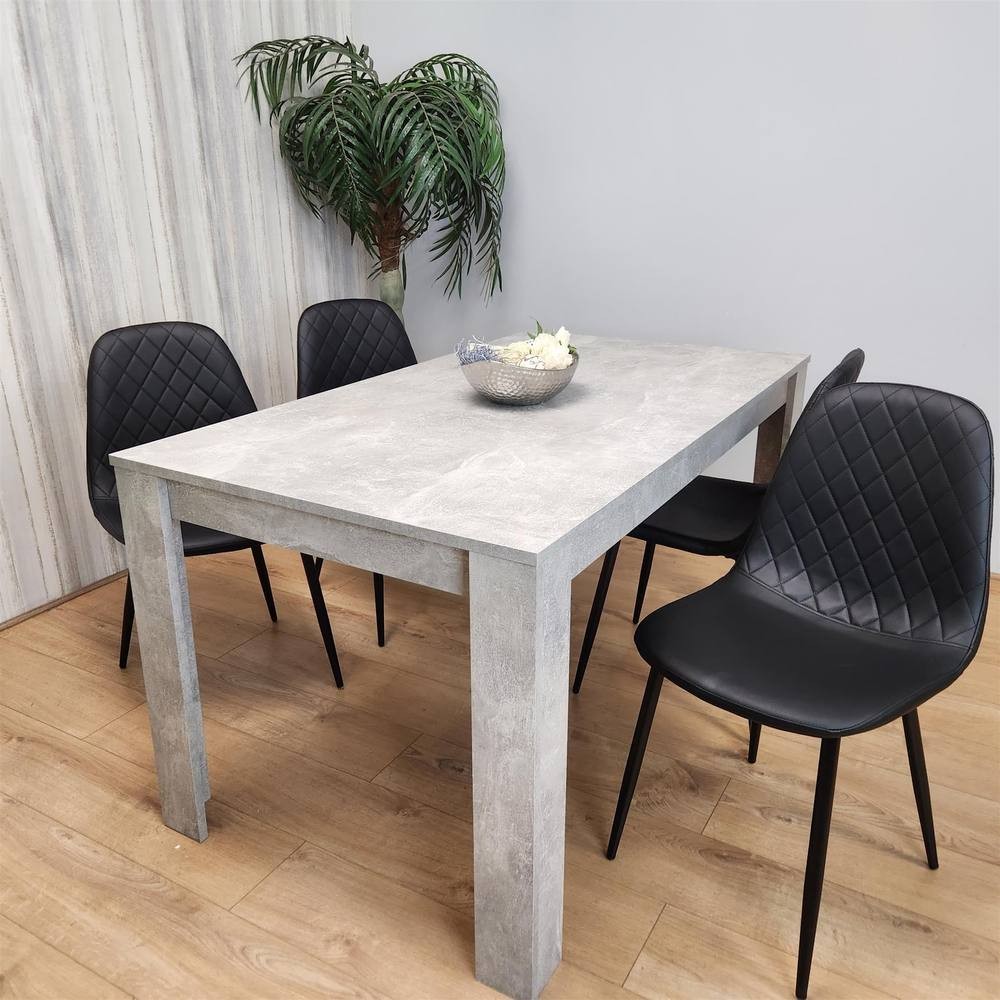 Grey wooden dining table with a smooth surface, accompanied by four black leather chairs featuring diamond-patterned backs, set against a light-colored wall and a potted plant.