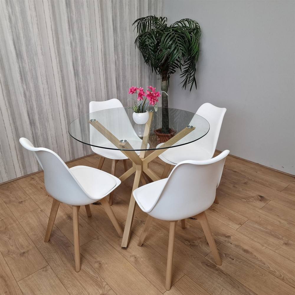 Clear glass dining table with a wooden tripod base, surrounded by four white plastic chairs with wooden legs, set against a light wood floor and a potted plant.