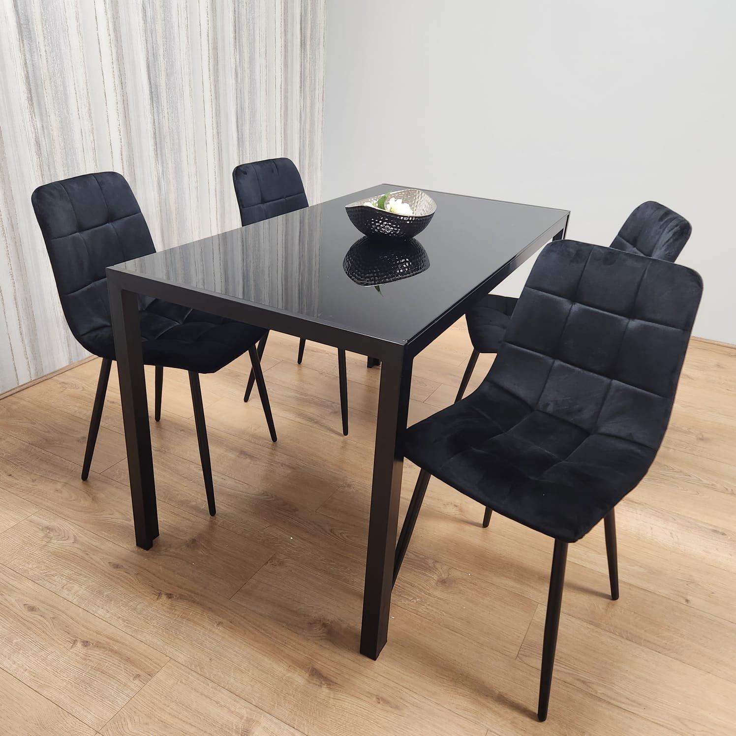 Black kitchen dining table with a glossy surface and four black tufted velvet chairs featuring sleek metal legs, set against a light wood floor and textured wall.