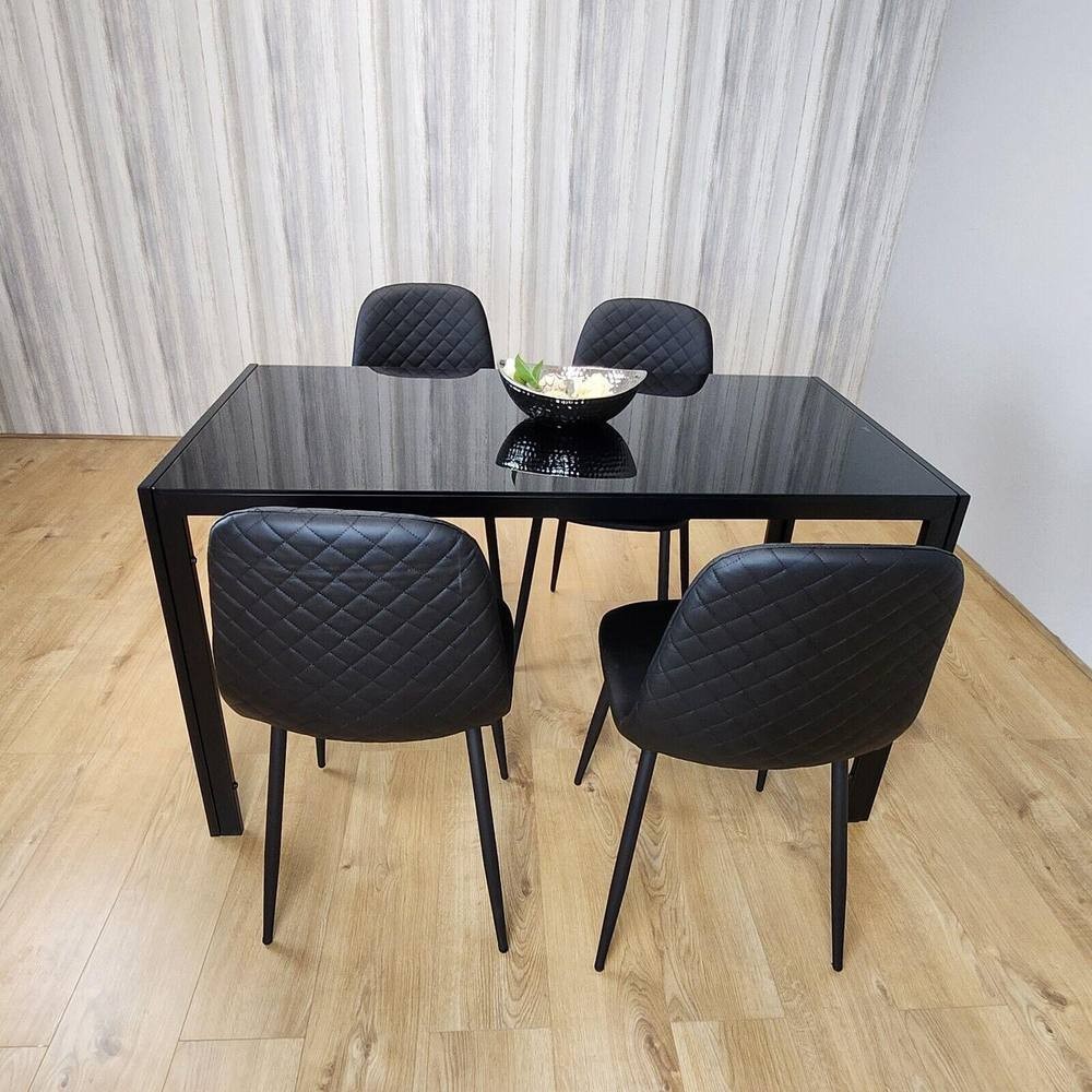 Modern black glass dining table with four black quilted chairs, set on a light wood floor, featuring a decorative bowl in the center.
