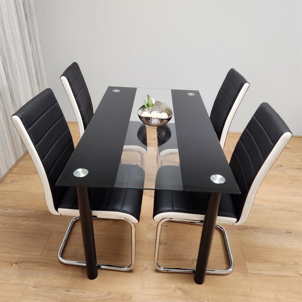 Modern black dining table with clear glass top and chrome accents, accompanied by four faux leather chairs in black and white, set on a light wood floor.