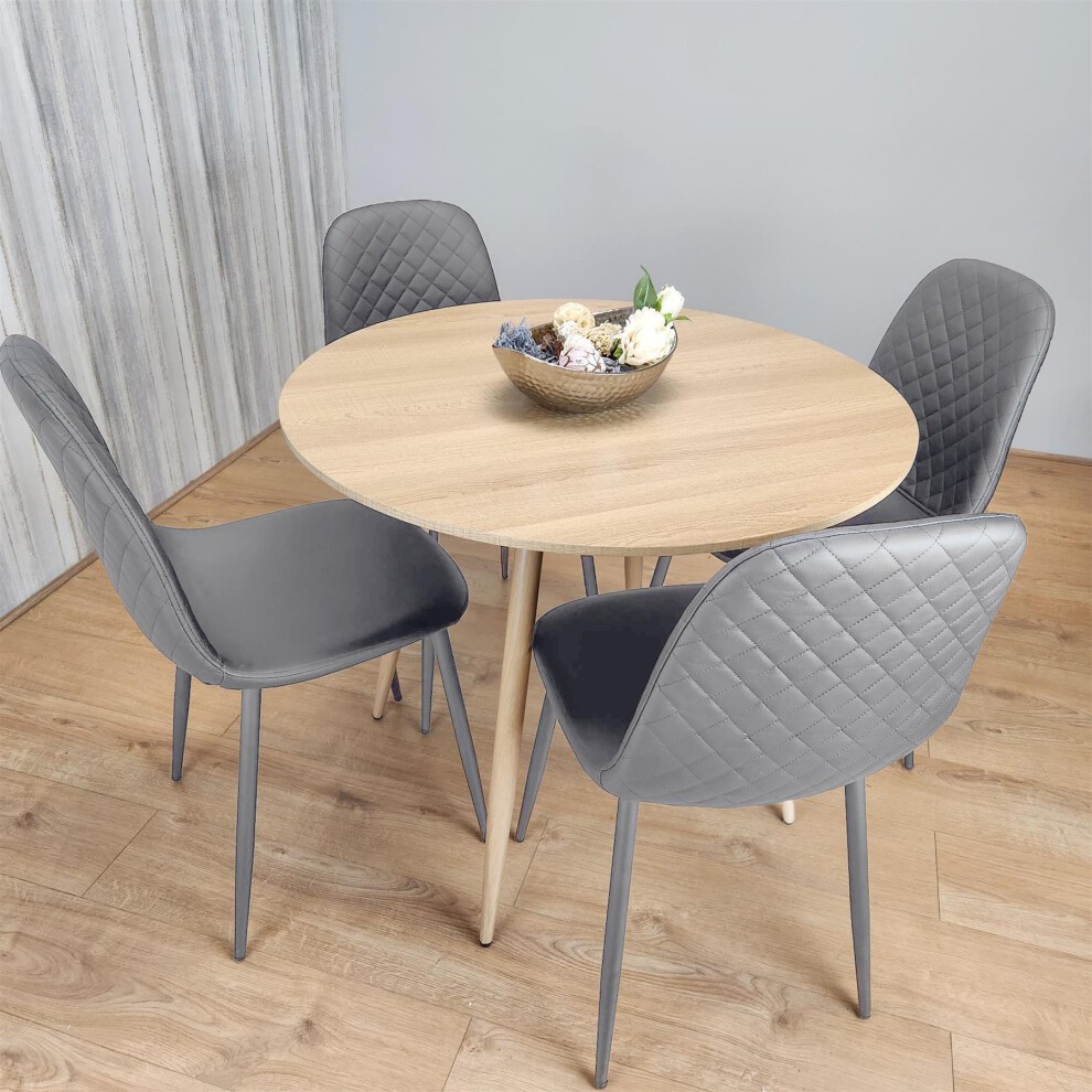 Modern round dining table with a light wooden top and four grey gem chairs featuring diamond-patterned upholstery and slender wooden legs, set against a neutral backdrop.
