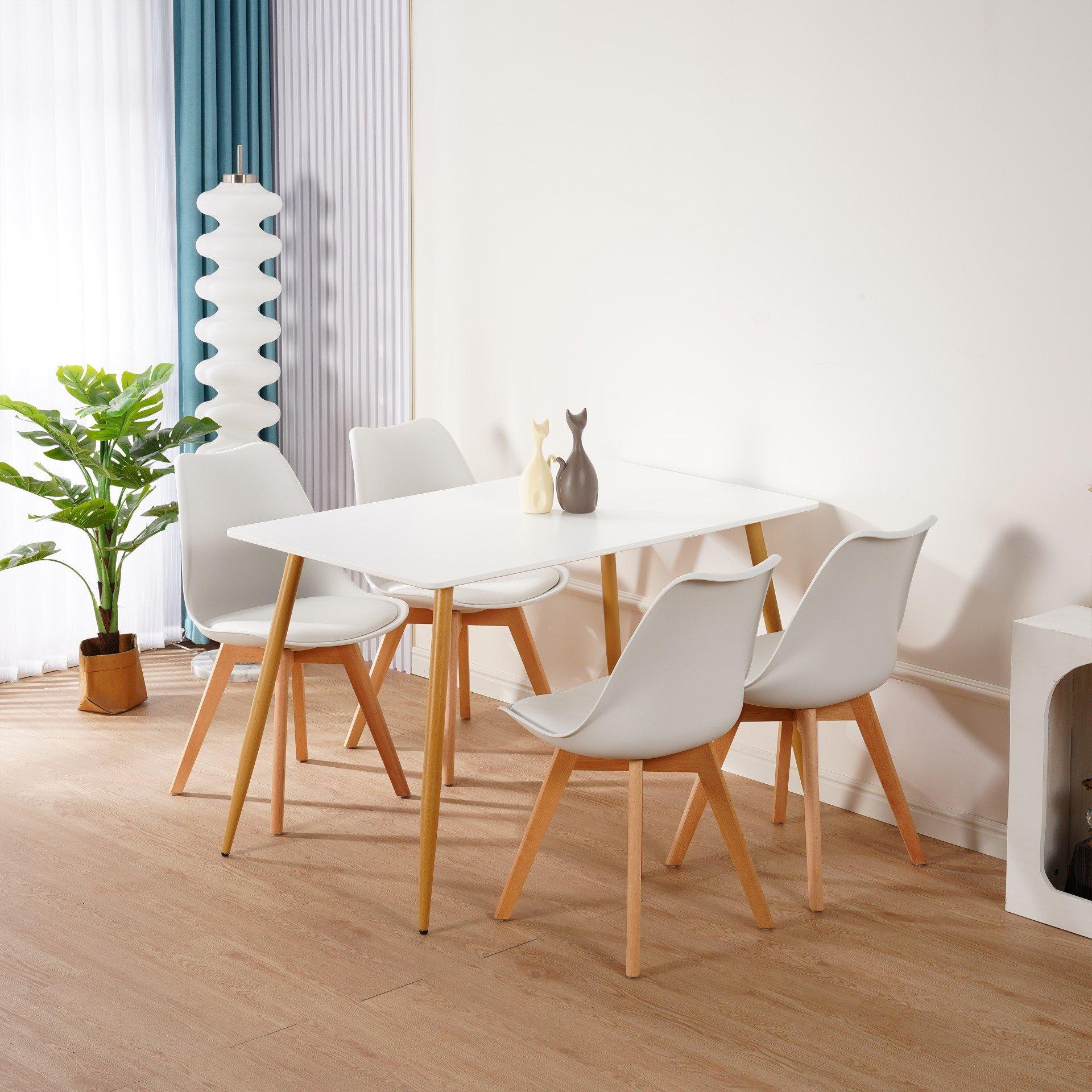 KOSY KOALA white dining table with four matching tulip chairs, featuring wooden legs, set against a light interior with a plant and decorative vases.