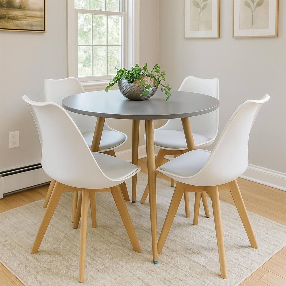 Grey round wood dining table surrounded by four white plastic leather chairs with wooden legs, complemented by a decorative plant in a bowl on the table.