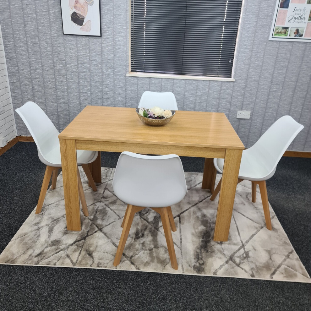 Beige KOSY KOALA dining table set featuring a wooden table with a smooth finish and four white plastic chairs with wooden legs, arranged on a patterned rug in a cozy dining space.