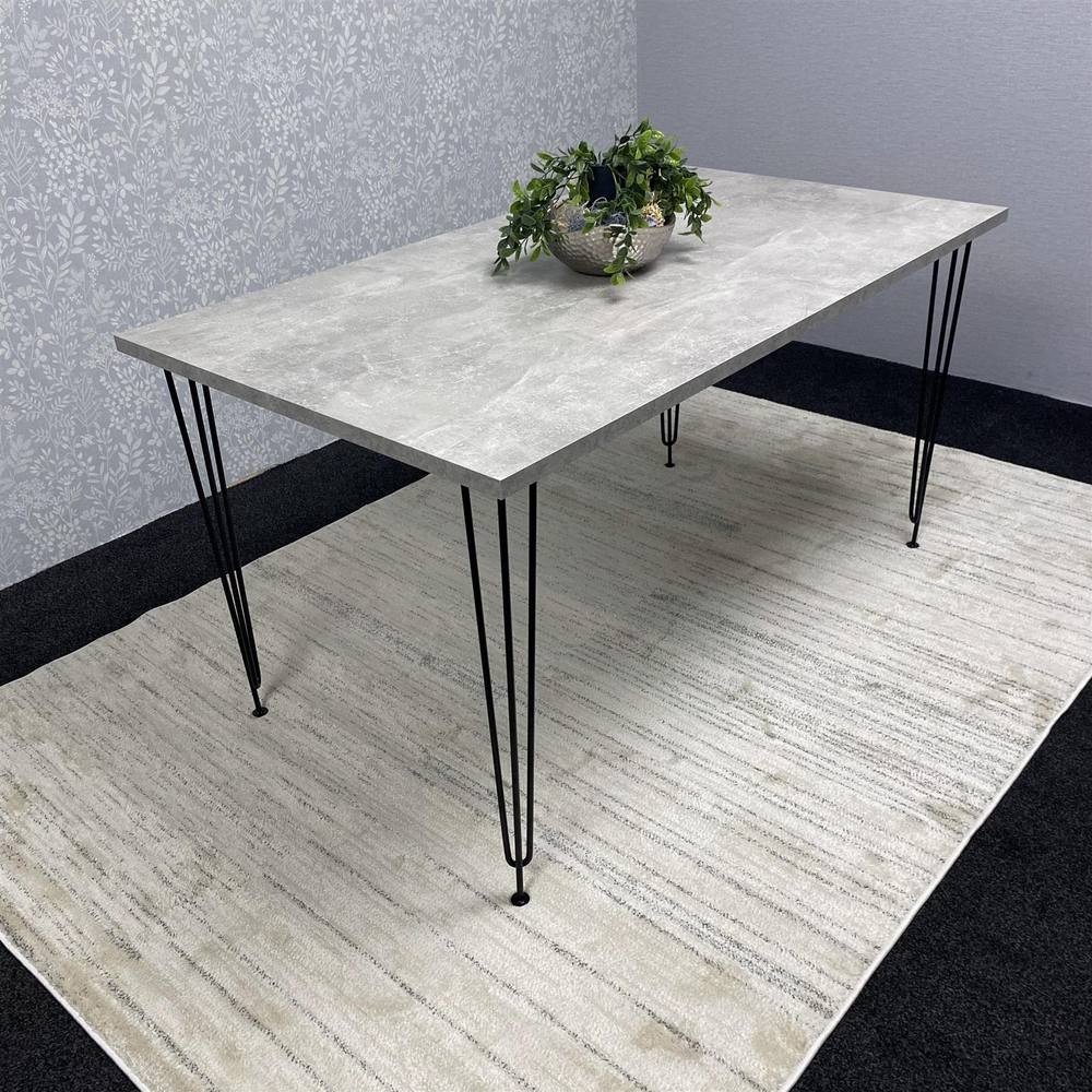 Modern grey rectangular dining table with a textured surface and black hairpin legs, placed on a light-colored rug, adorned with a potted plant centerpiece.