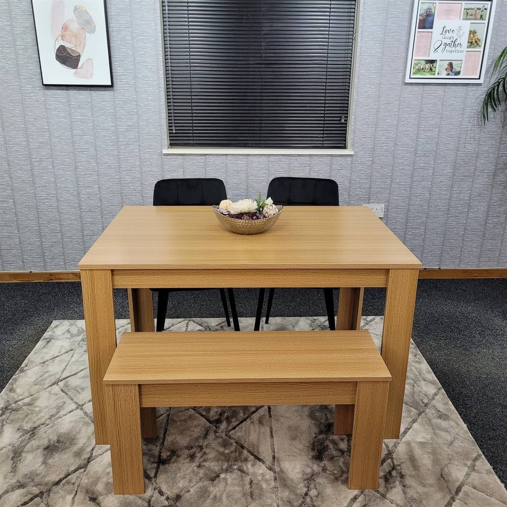 Beige KOSY KOALA dining table set featuring a rectangular table, two black chairs, and a matching bench, all set on a patterned rug with a decorative bowl centerpiece.