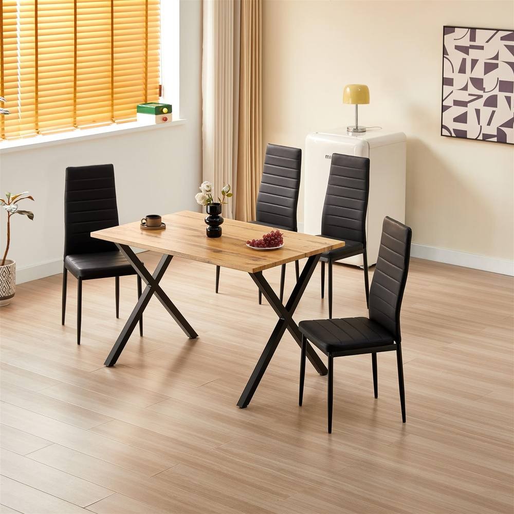 Kosy Koala wooden dining table in brown with a light wood finish, paired with four black leather chairs, set in a bright room with wooden flooring and large windows.
