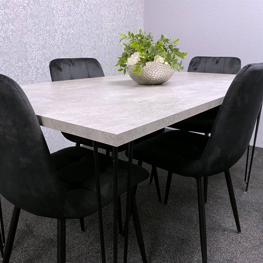 Modern grey dining table with a smooth surface, surrounded by four black velvet chairs, featuring slender black legs and a decorative plant centerpiece.