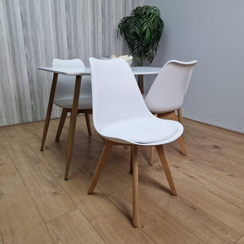 KOSY KOALA dining table set features a sleek grey table with four white chairs, each with wooden legs, set against a light wooden floor and a green plant backdrop.