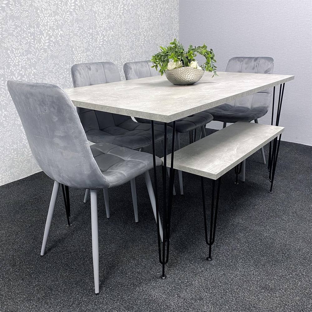 Modern dining table set featuring a light grey tabletop, four grey velvet chairs with sleek legs, and a lower shelf, set against a textured wall.