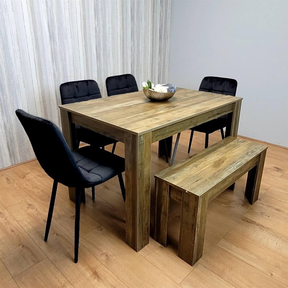 Modern dining table in brown wood with four black velvet chairs and a matching bench, set against a light-colored wall and wooden floor.