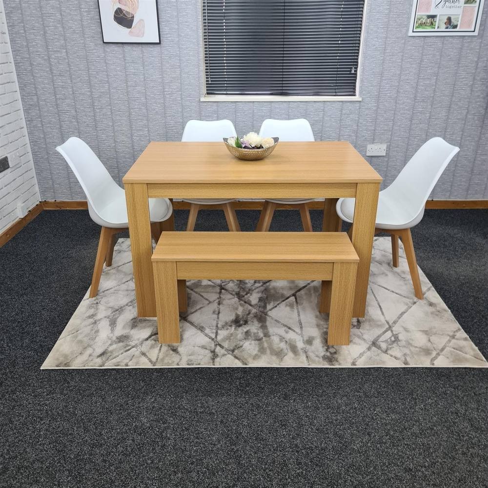 KOSY KOALA dining table set featuring a light wood table with a beige finish, accompanied by four white chairs and a matching bench, all on a patterned rug.