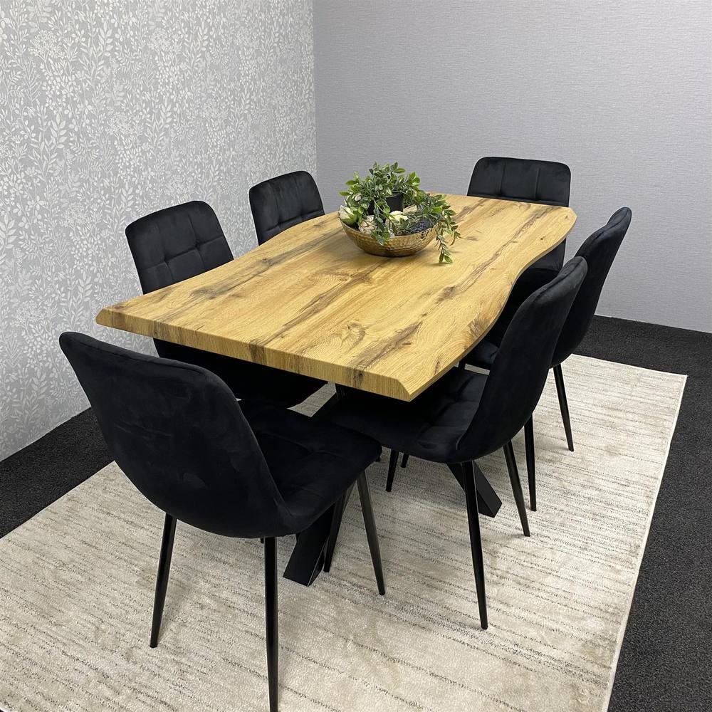 Modern dining table set featuring a brown wooden table with a natural finish and six black velvet chairs, all set on a light rug against a textured wall.