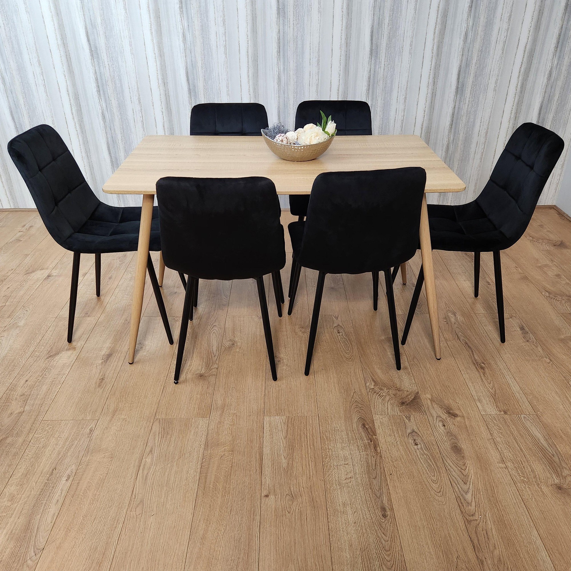 Rectangle oak effect dining table with six black velvet tufted chairs, featuring a smooth surface and sleek wooden legs, set on a light wooden floor with a decorative bowl centerpiece.