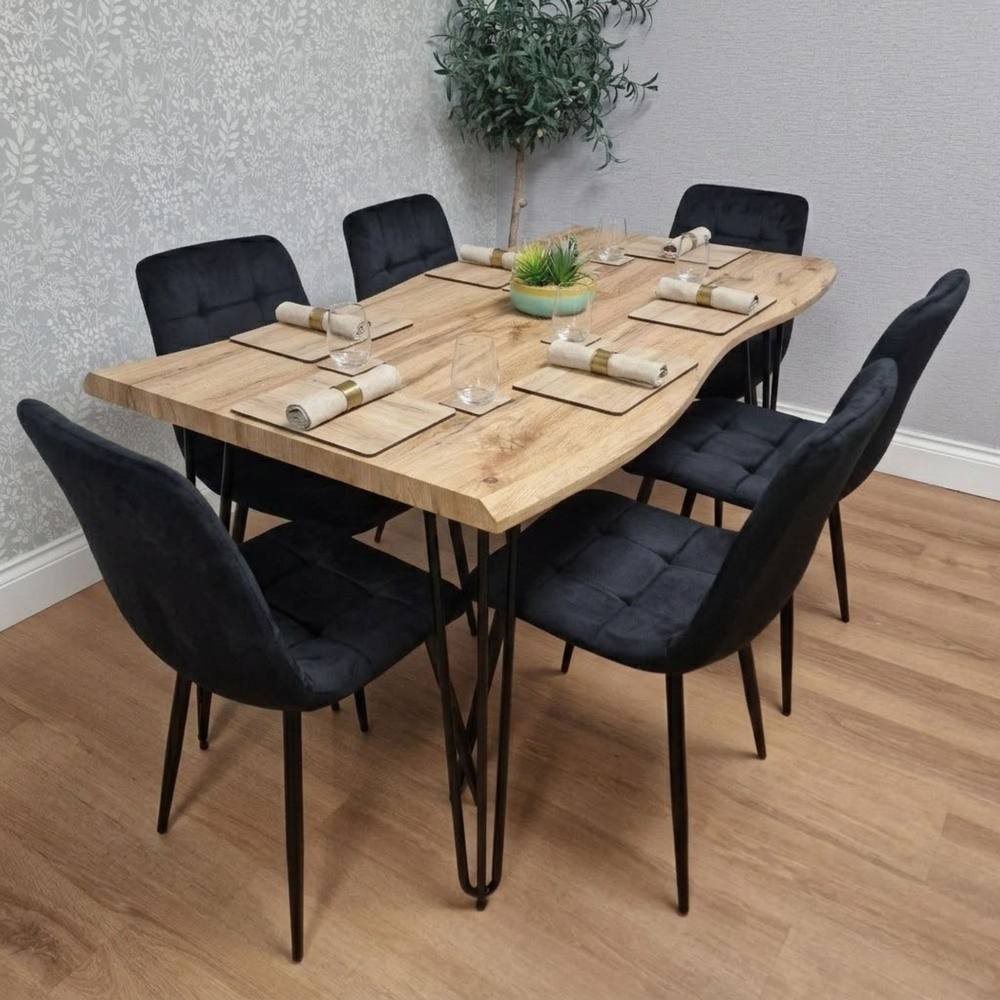 Stylish wooden dining table with a natural brown finish and six black velvet chairs, featuring sleek black metal legs, set with tableware and a small green plant centerpiece.
