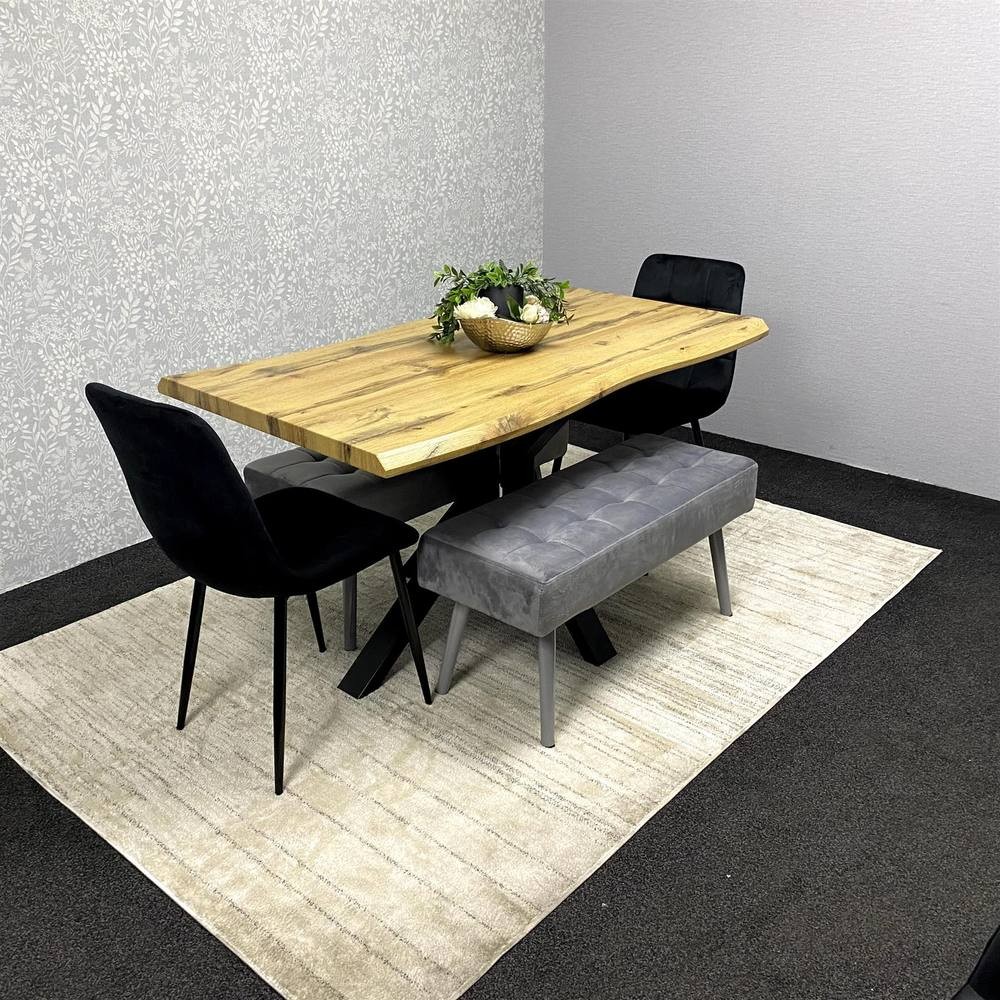 Kosy Koala wooden dining table in brown with a natural finish, accompanied by two black velvet chairs and grey padded benches, set on a light rug against a textured wall.