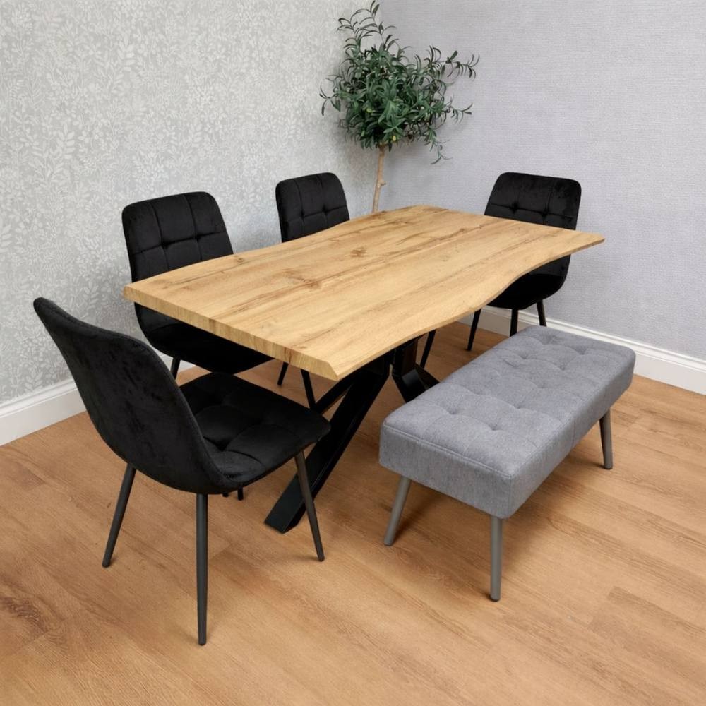 Kosy Koala wood dining set features a natural wood table with a unique shape, four black velvet chairs, and a grey velvet bench, all set against a light grey wall and wooden floor.