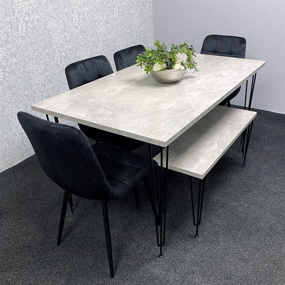 Modern grey dining table with a smooth surface, supported by black metal legs, accompanied by four black velvet chairs and a decorative plant centerpiece.