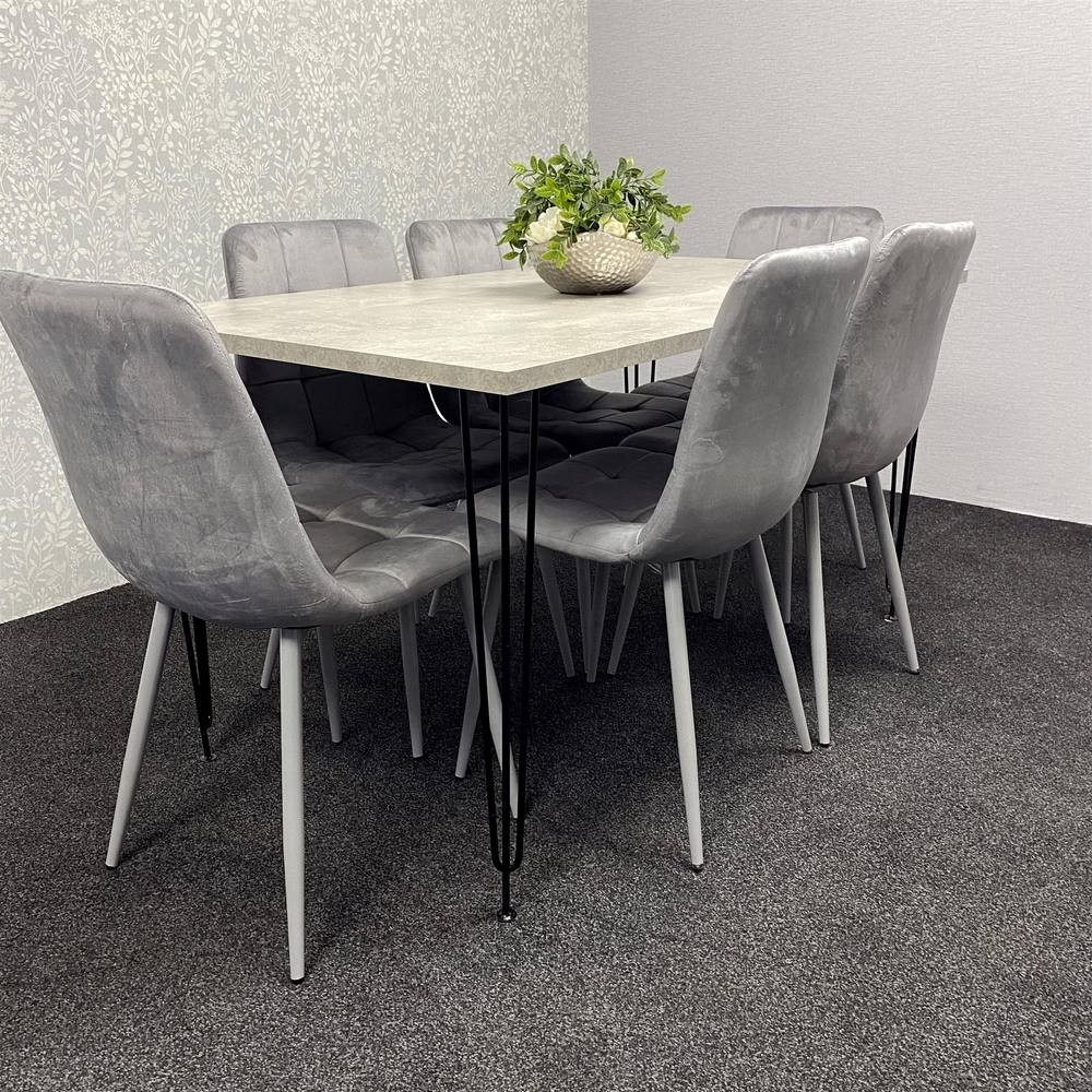 Modern grey dining table with a smooth surface and six plush grey velvet chairs, featuring sleek black metal legs, set against a light-patterned wall.