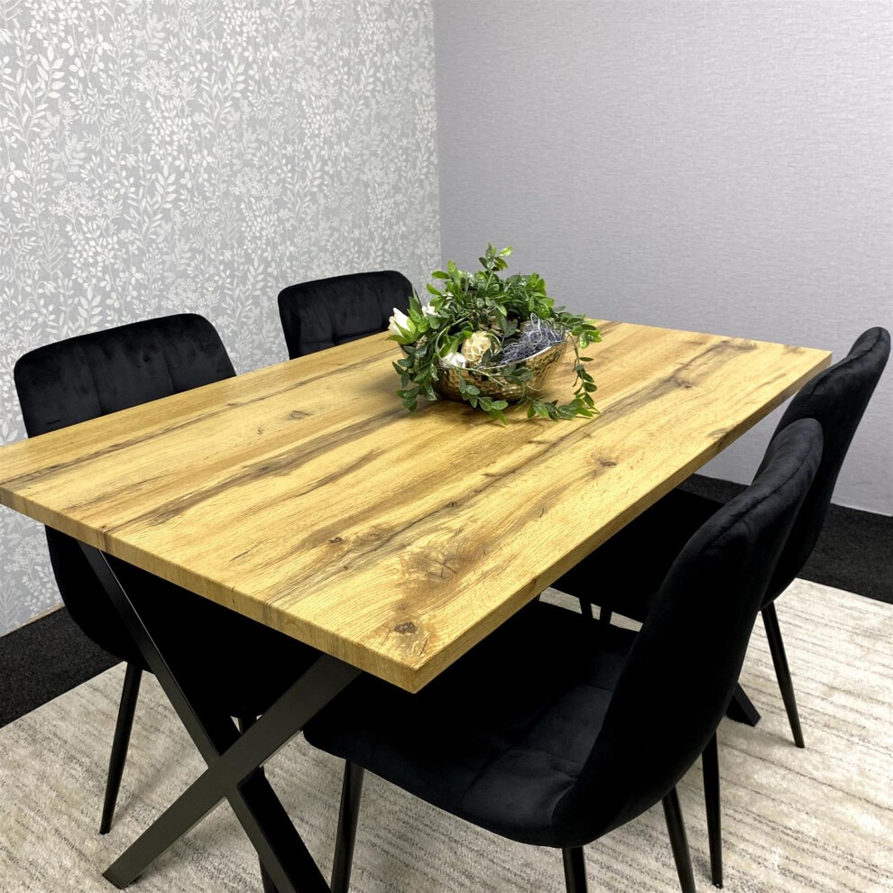 Stylish wooden dining table with a natural brown finish, accompanied by four black velvet chairs and a decorative plant centerpiece.