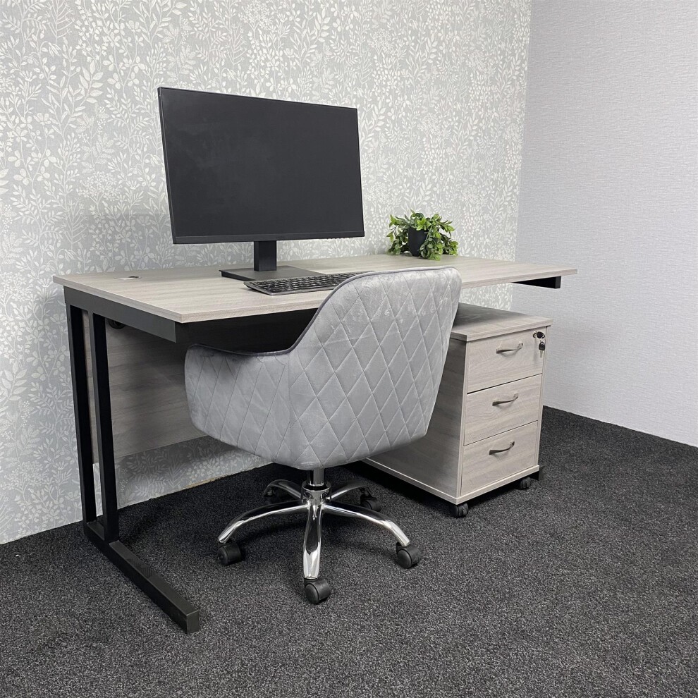 L-shaped grey office desk with a black velvet upholstered chair, featuring diamond stitching, and a storage drawer unit on the right.