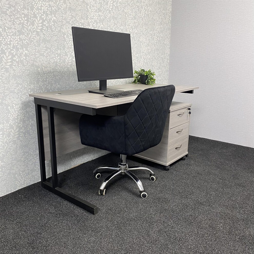 Grey office desk with a sleek design, black velvet upholstered chair featuring a diamond pattern, and a matching drawer unit, set against a floral wallpaper background.