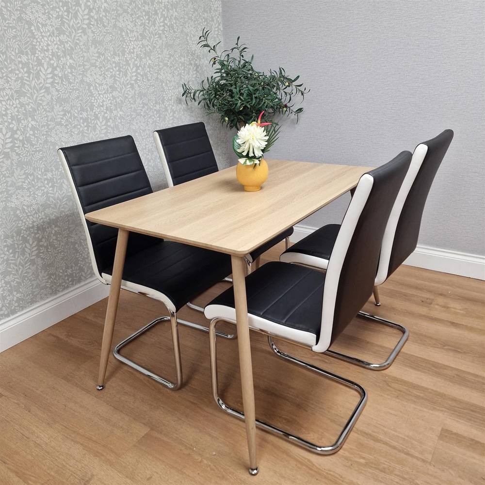 Modern rectangle dining table in light wood with four black faux leather chairs featuring white accents, complemented by a small vase of flowers on the table.