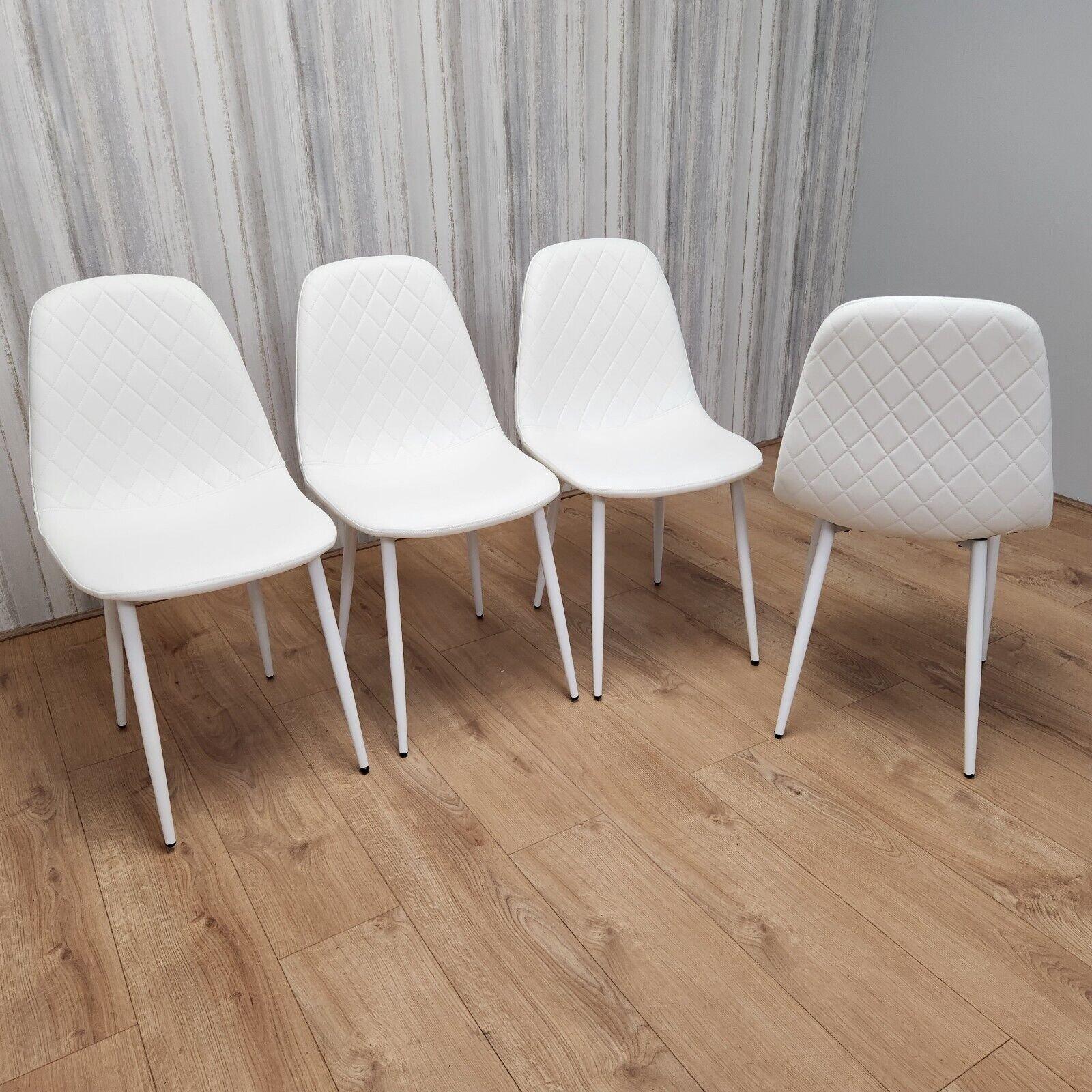 Set of four white dining chairs with stitched faux leather seats, featuring soft padding and sleek, tapered legs, arranged on a wooden floor against a light wall.