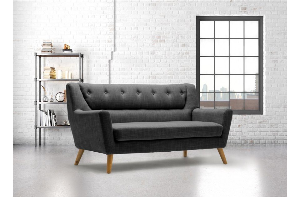 Modern retro-style 3-seater sofa in dark grey fabric with wood legs, featuring button detailing and a sleek silhouette, set against a bright, industrial-style room.