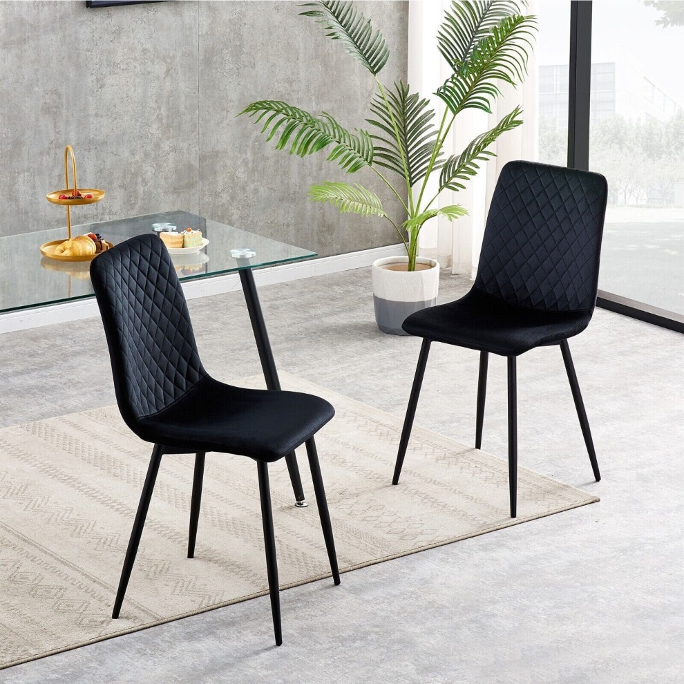 Set of 2 black velvet dining chairs with diamond quilted pattern, featuring sleek black metal legs, placed near a glass table and a potted plant in a modern interior setting.