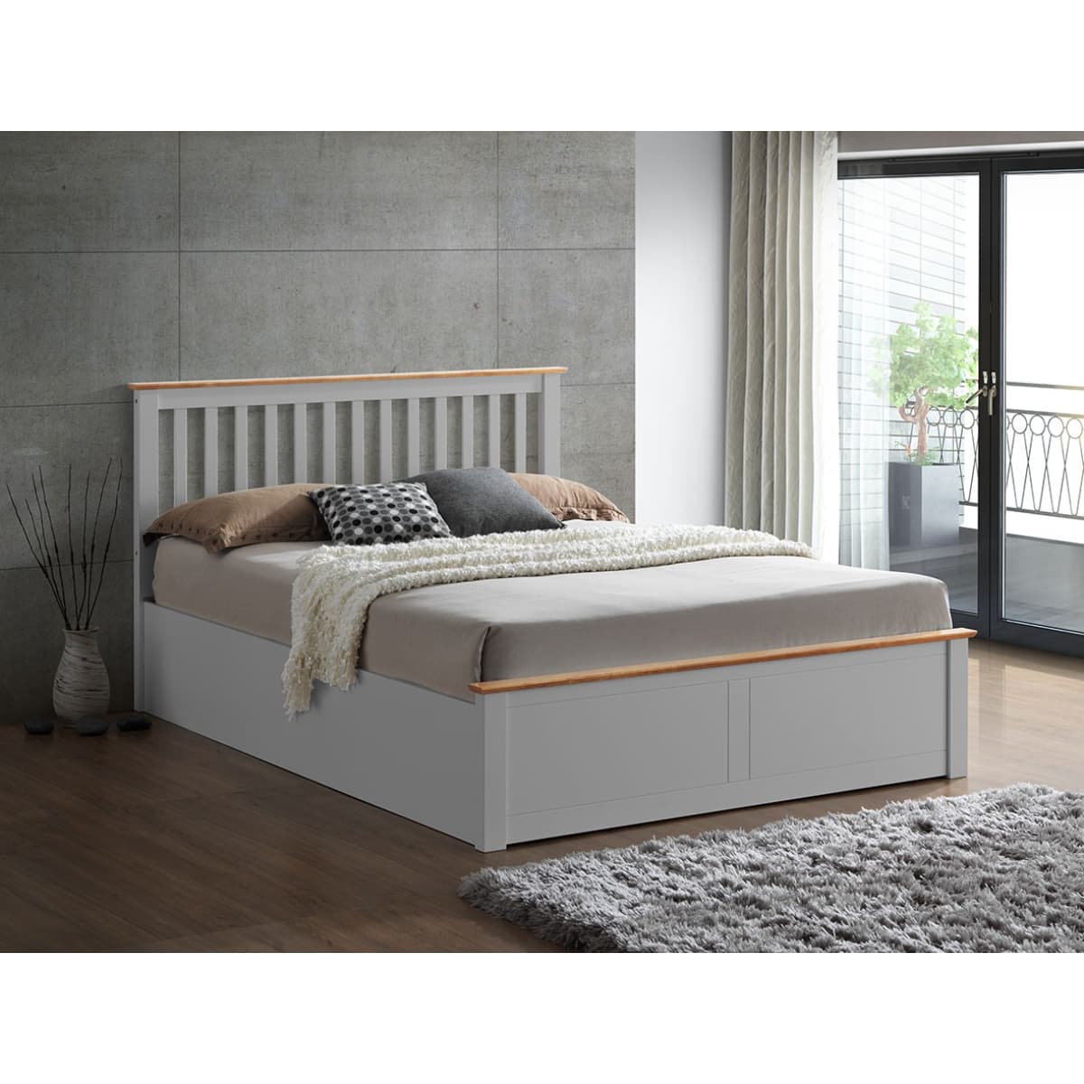 Grey wooden Ottoman bed with a slatted headboard, king size, featuring a light wood trim, plush bedding, and decorative pillows, set against a modern interior with large windows.