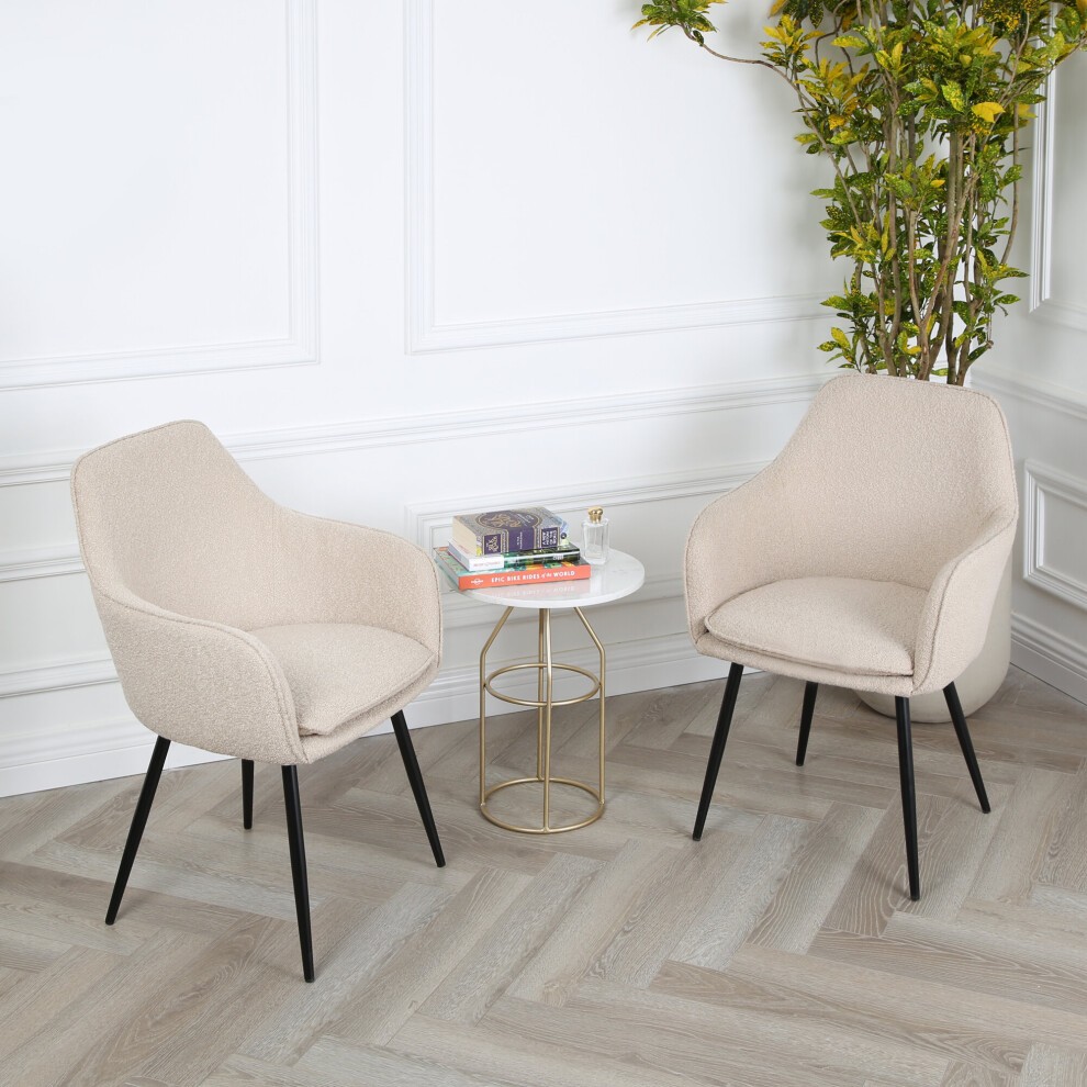 Occasional chair in boucle fabric featuring a beige and cream color scheme, with sleek black legs, accompanied by a small round marble-topped table and greenery in the background.