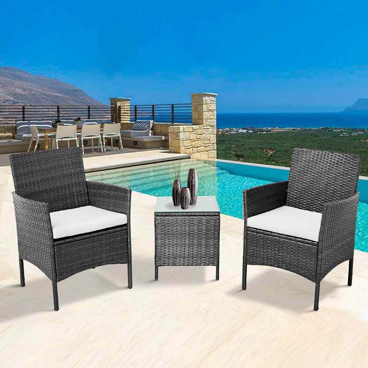 Three-piece bistro set featuring two black rattan chairs with cream cushions and a matching square table, set against a scenic poolside backdrop.
