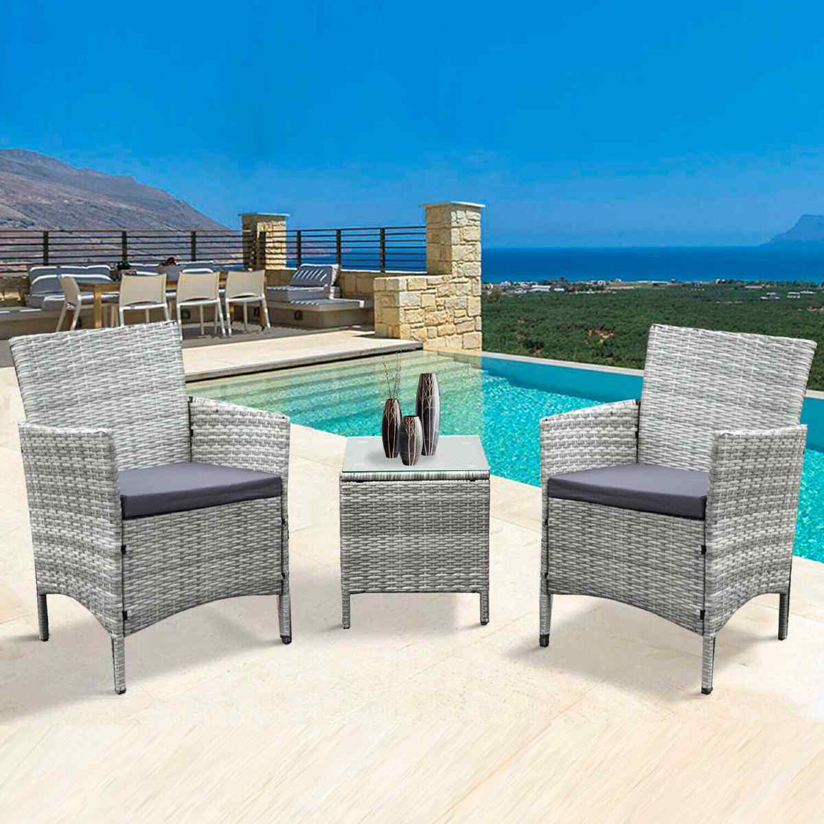 Grey rattan bistro set featuring two armchairs with gray cushions and a matching square table, set against a scenic poolside backdrop.