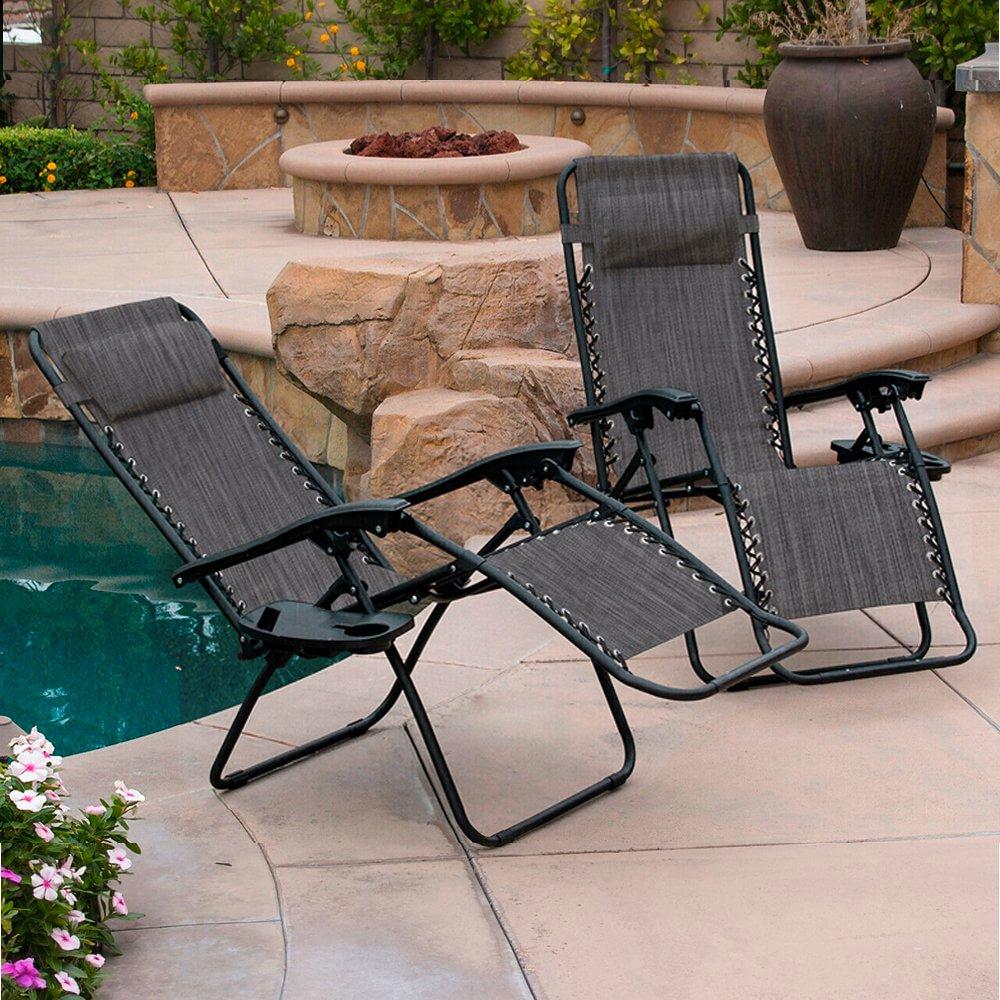 Two Neo Zero Gravity Recliner Garden Sun Loungers in dark gray fabric with black metal frames, positioned near a pool and surrounded by stone and greenery.